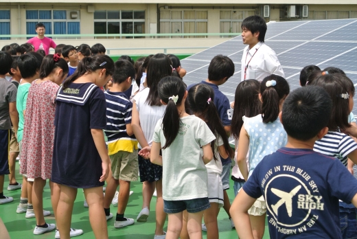 埼玉県志木市の小中11校の太陽光発電屋根貸し事業に参画。パネルをバックに小学生の前で環境授業。